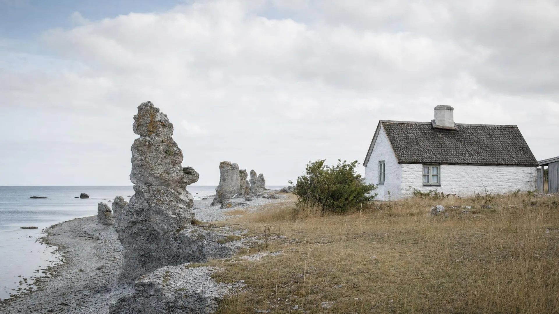 Gotländsk kust med raukar och vitkalkat stenhus i Gotlands län