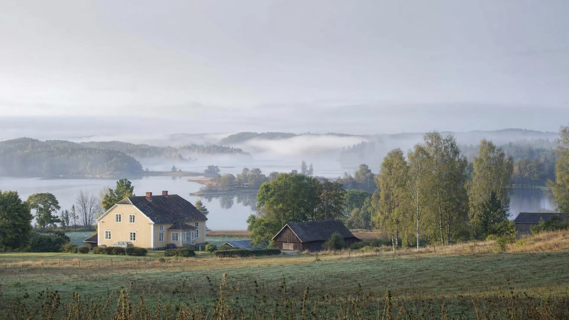 Sörmländskt landskap med sjö, gul gårdsbyggnad och blandskog i Södermanlands län